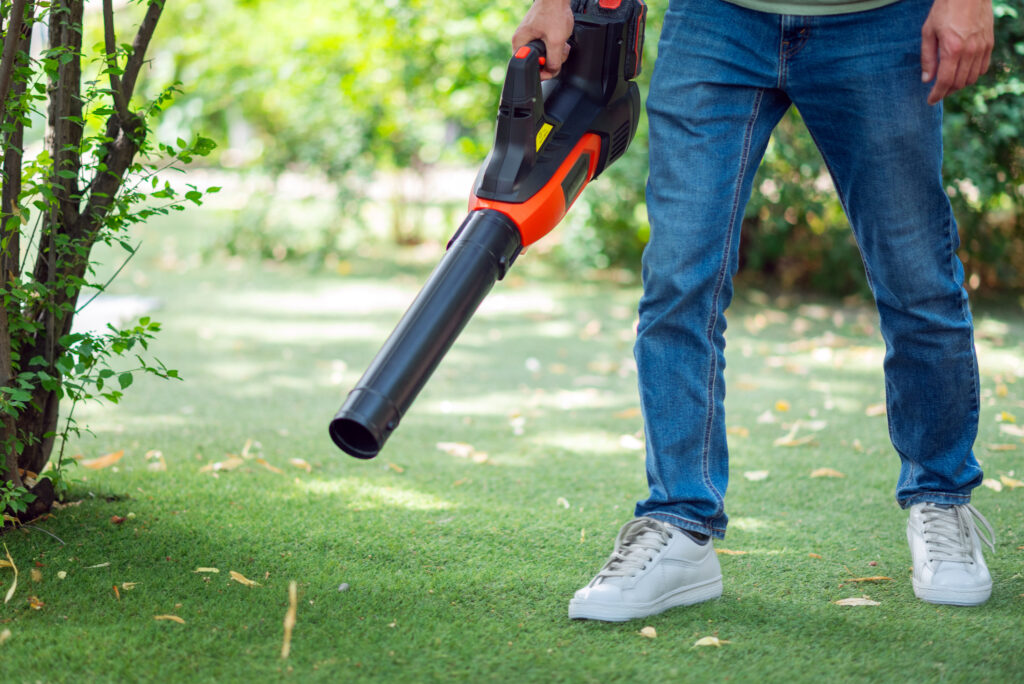 Homeowner using a leaf blower to clear autumn leaves from artificial turf in Dallas-Fort Worth, showing simple fall maintenance